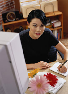 A woman with dark hair looks up while writing on a notepad